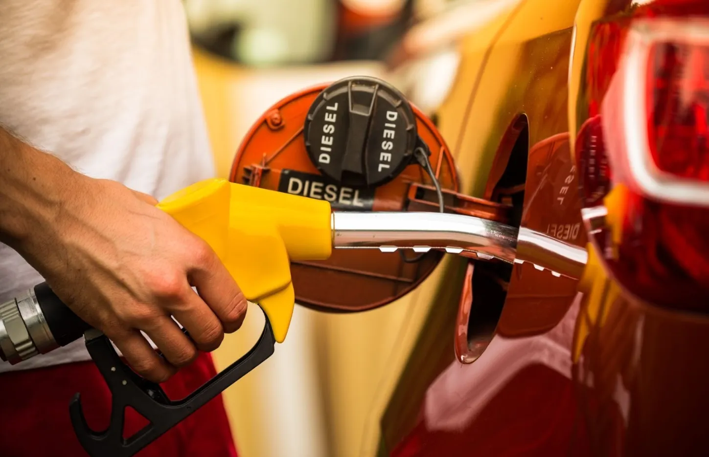 Tankovanie dieselového auta – ruka drží žltú palivovú pištoľ zasunutú do nádrže označenej „diesel“ na červenom vozidle.