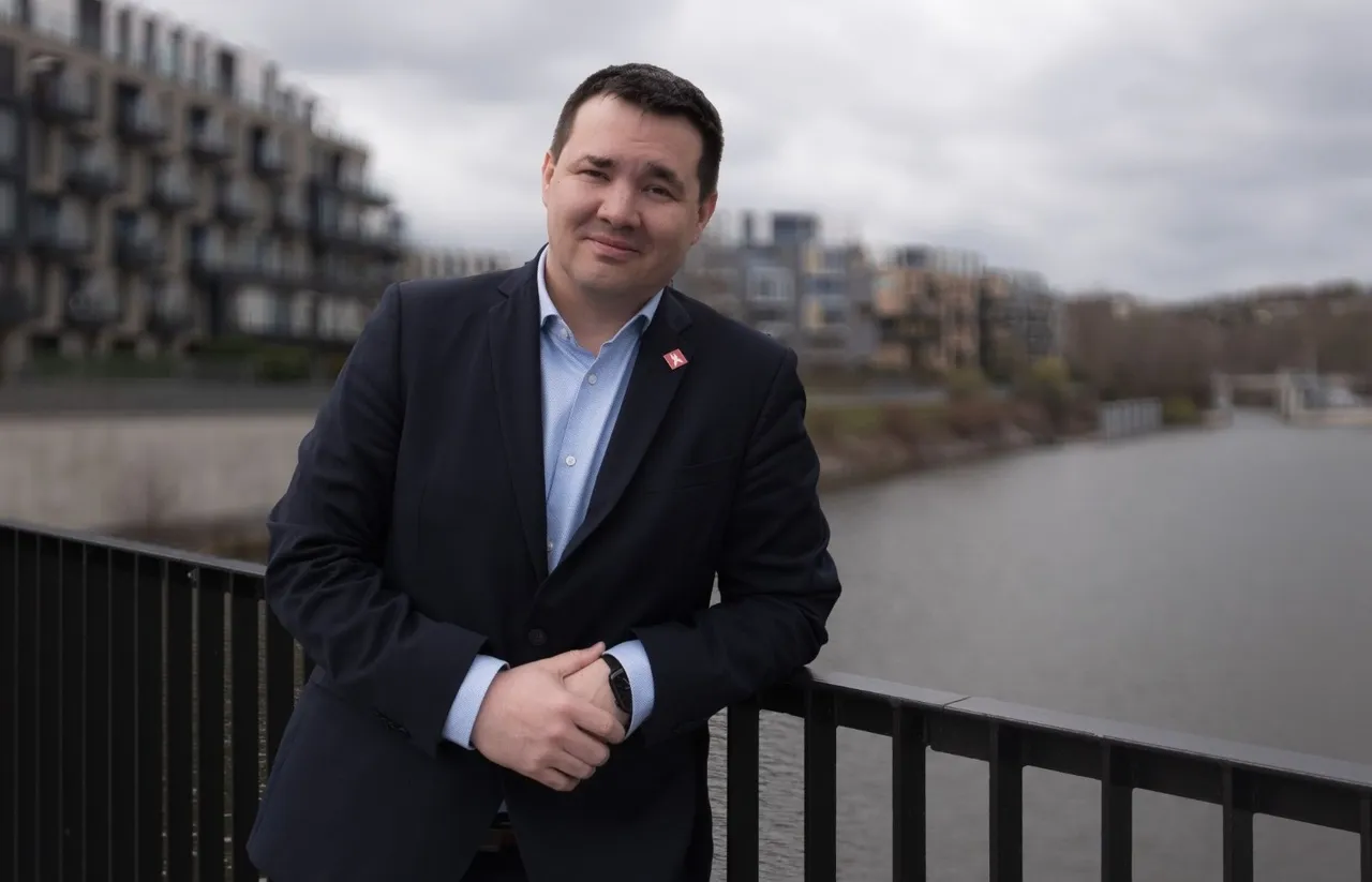 Vladimír Holovka, zástupca spoločnosti XTB, stojí opretý o zábradlie mosta s výhľadom na rieku a moderné bytové domy v pozadí
